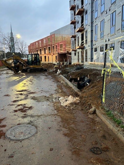 Construction site: excavator on muddy road next to unfinished apartment buildings. Cloudy day.