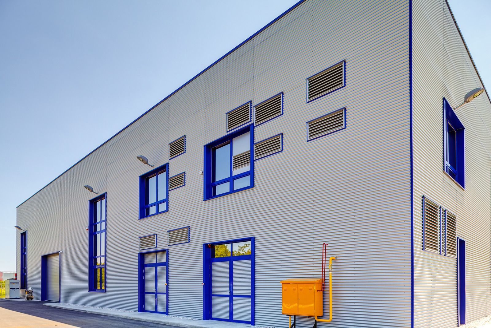 Modern building with corrugated metal siding, blue window frames, and air vents against a clear sky.