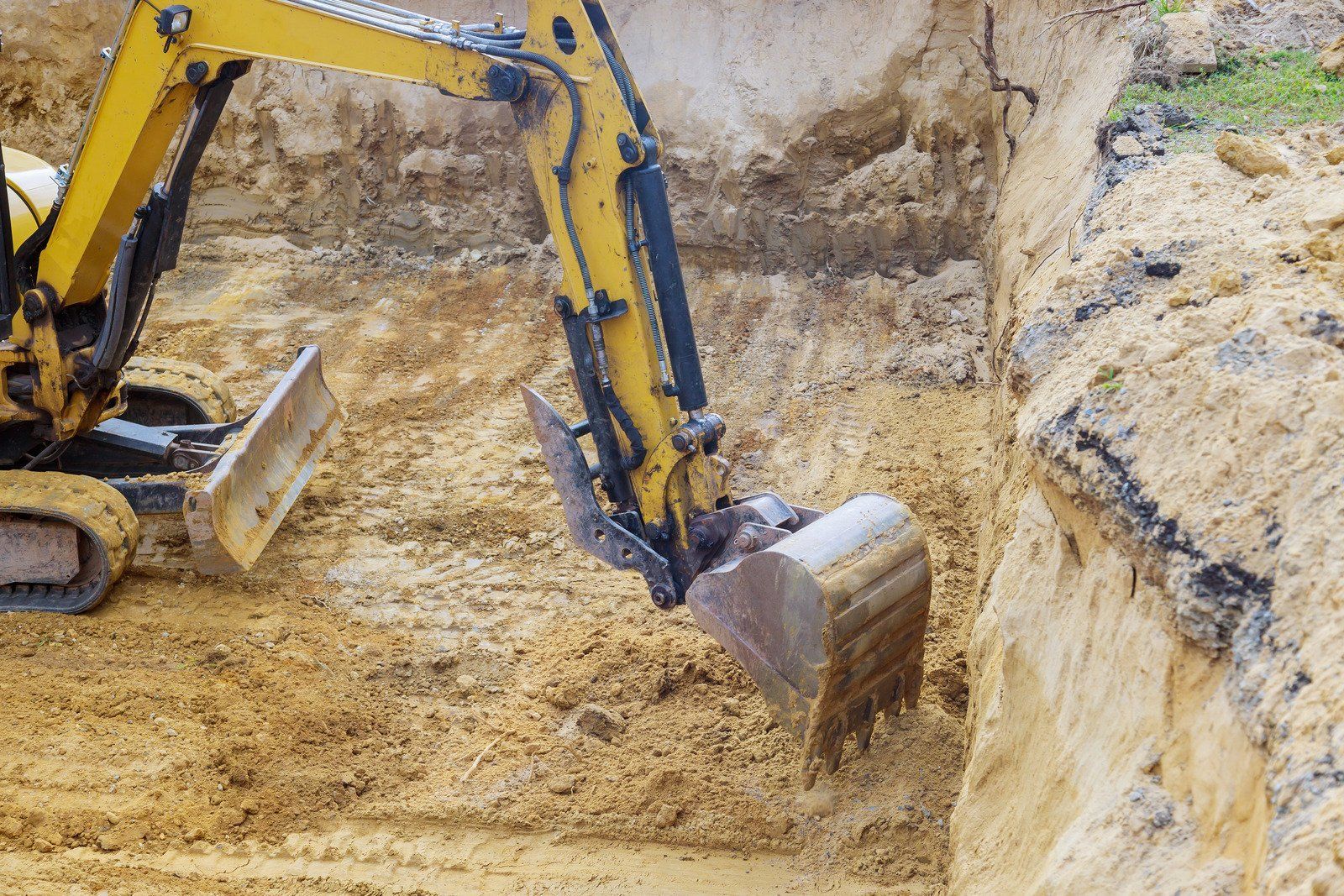 Yellow excavator digging into a brown earthen trench.