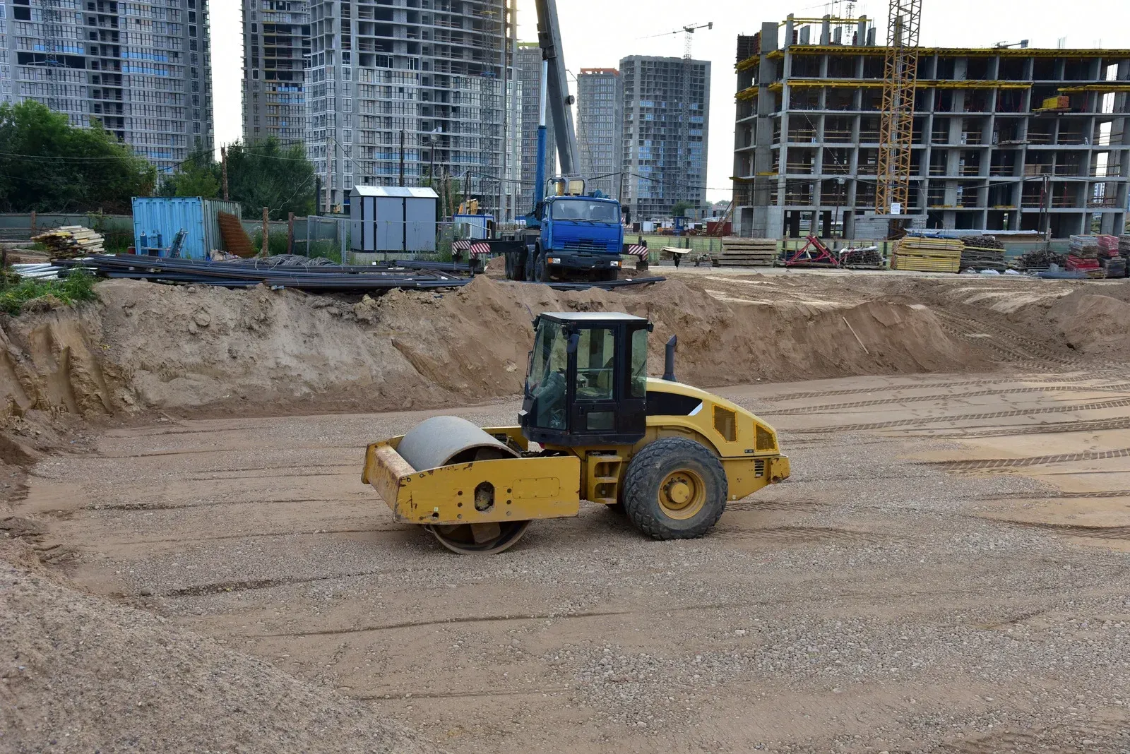 Yellow road roller compacting earth on a construction site with unfinished buildings in the background.