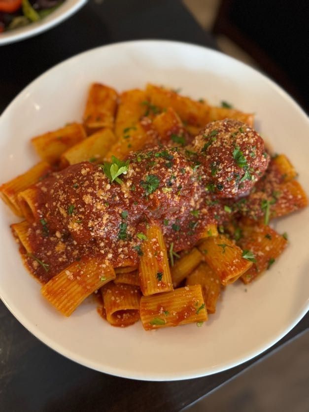 Pasta in red sauce topped with herbs and grated cheese on a white plate