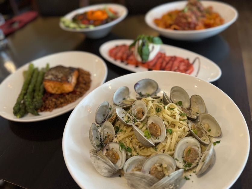 Plated seafood pasta with clams in the foreground, with several other dishes on a table behind it