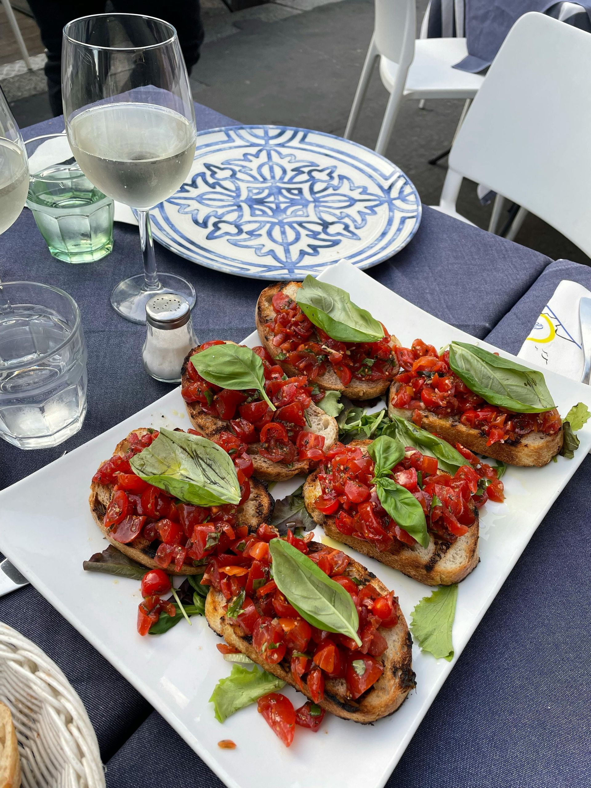 Plated bruschetta with tomatoes and basil on a café table beside a wine glass and water glass