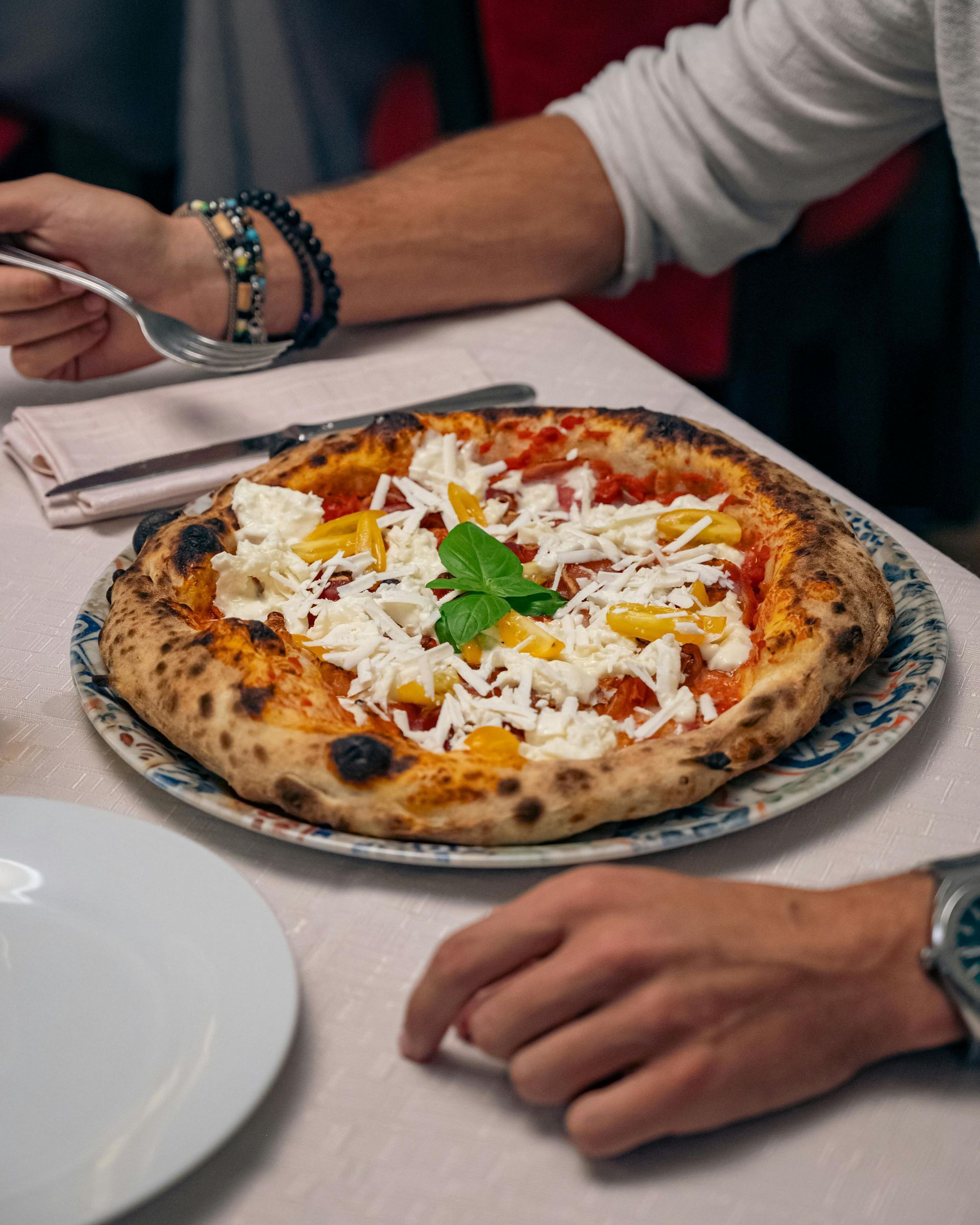 Pizza on a plate at a table, with hands reaching nearby in a casual dining setting