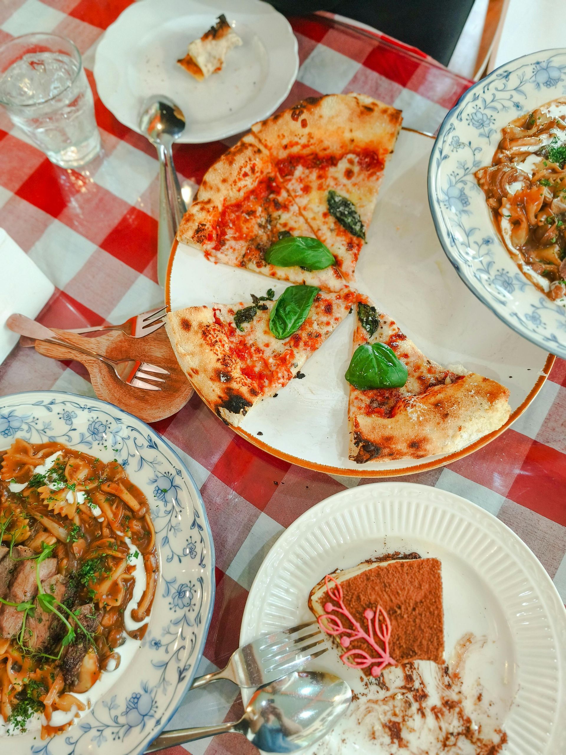 Italian meal spread on a red-and-white checkered tablecloth with pizza, pasta, soup, and dessert.