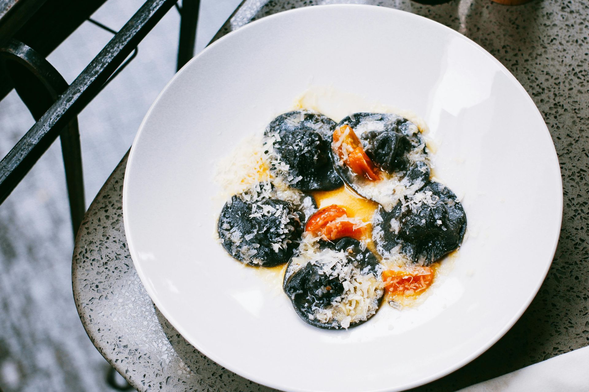 White plate with four dark dumplings topped with grated cheese and orange sauce on a table