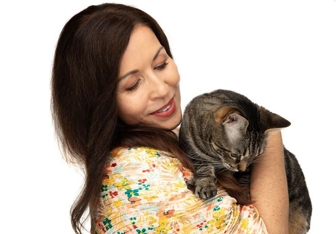 A woman is holding a cat in her arms and smiling.