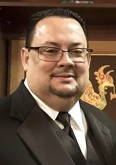 A man with glasses and a beard is wearing a suit and tie.