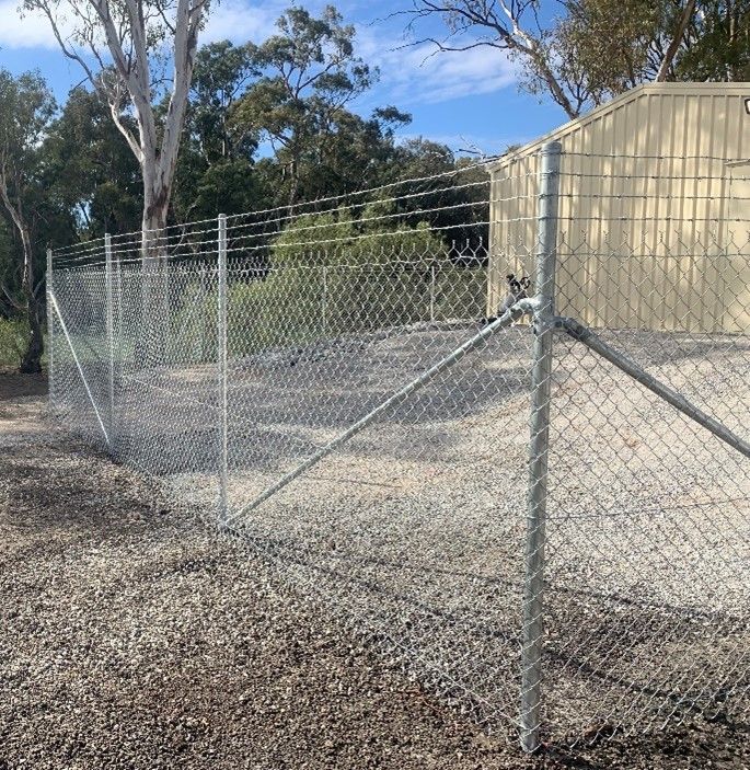 A chain link fence is surrounded by gravel and trees.
