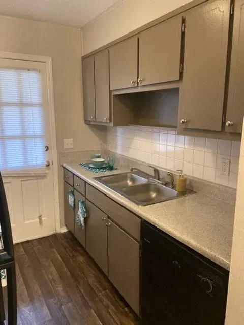 A kitchen with gray cabinets, a double sink, white tile, and a door to the left.