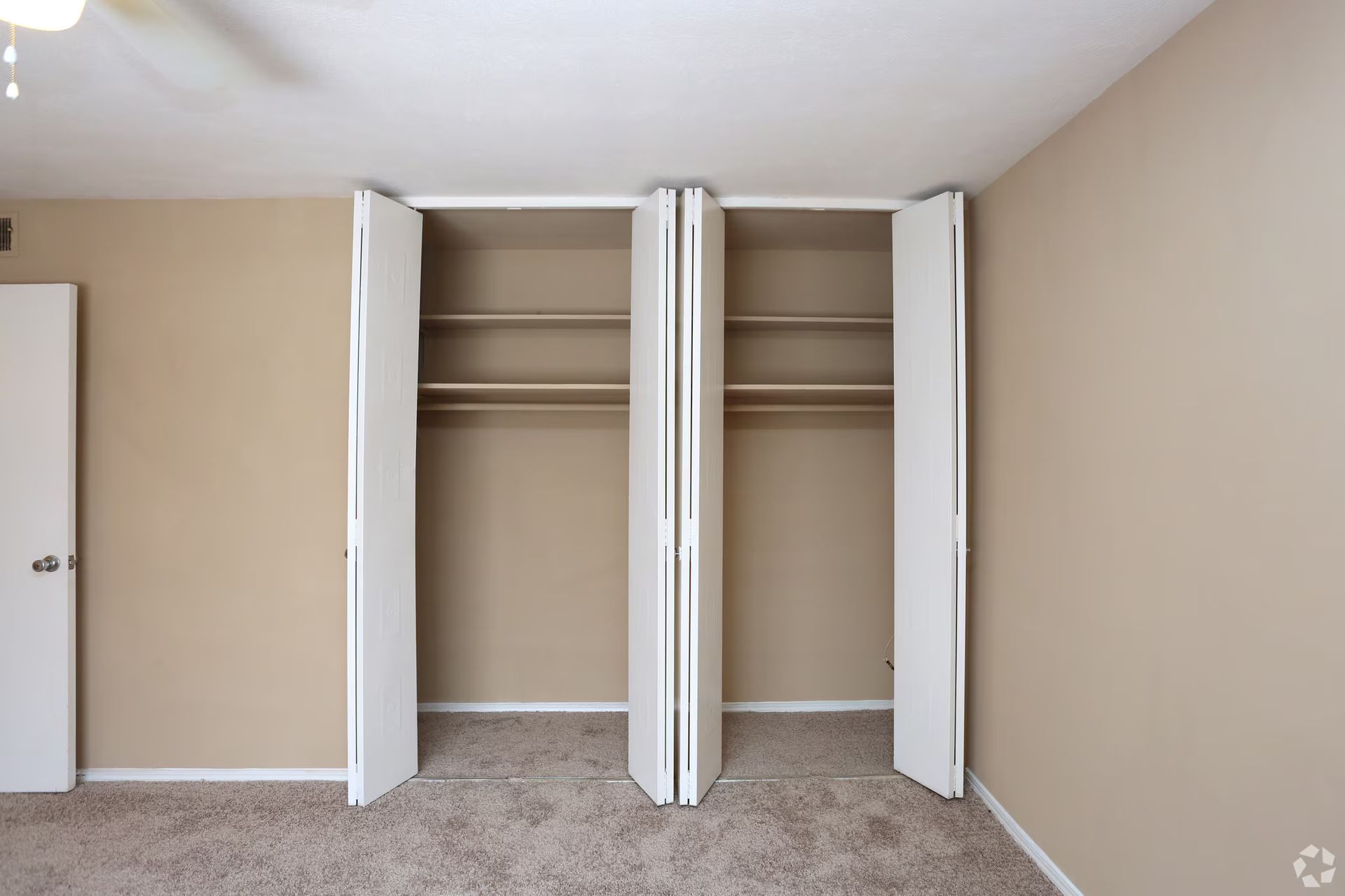 Empty bedroom with two mirrored closets, tan walls, and beige carpet.