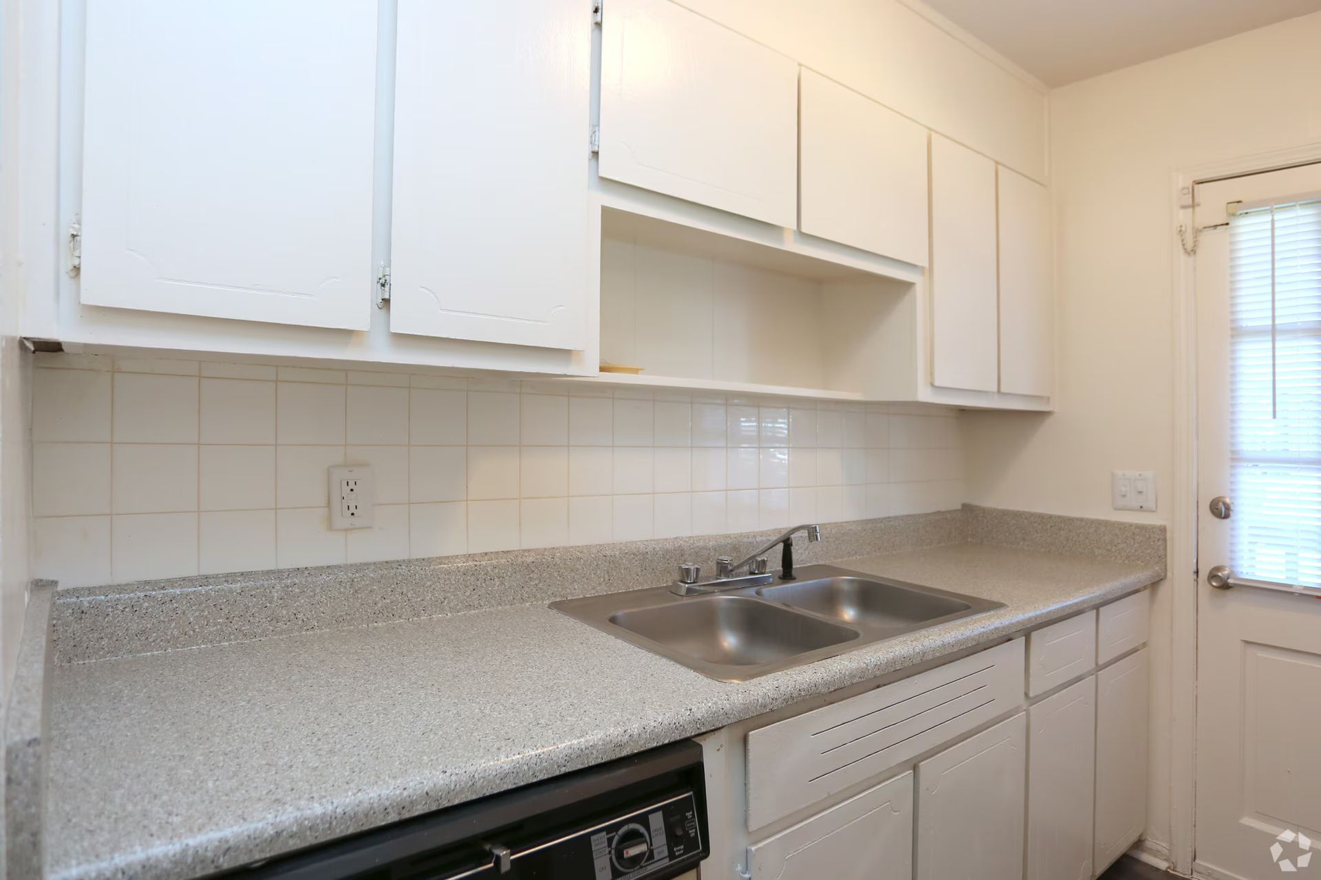 White kitchen cabinets, countertop, and sink; door with blinds on the right.