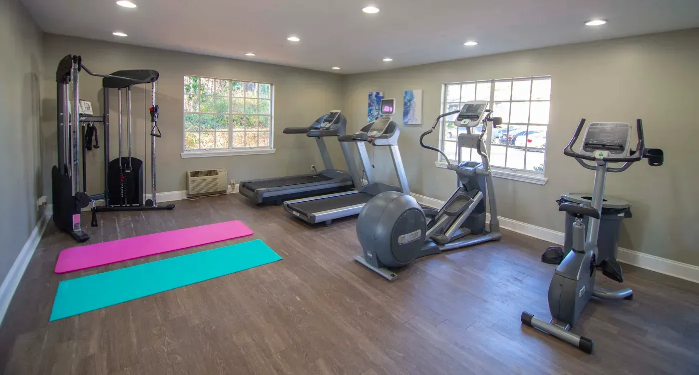 Gym with exercise equipment, including treadmills, elliptical, stationary bike, and weight machine.