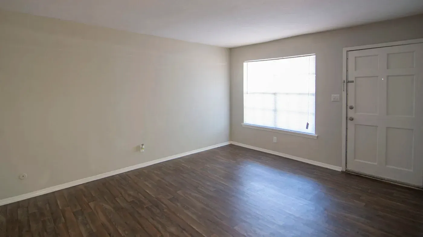 Empty room with wood-look floor, window, and white door; beige walls.
