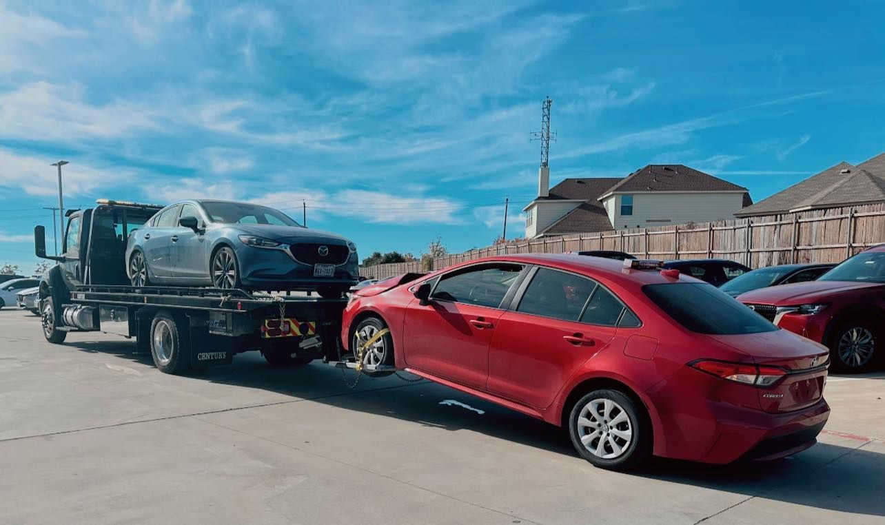 A red car is being towed by a tow truck in a parking lot.