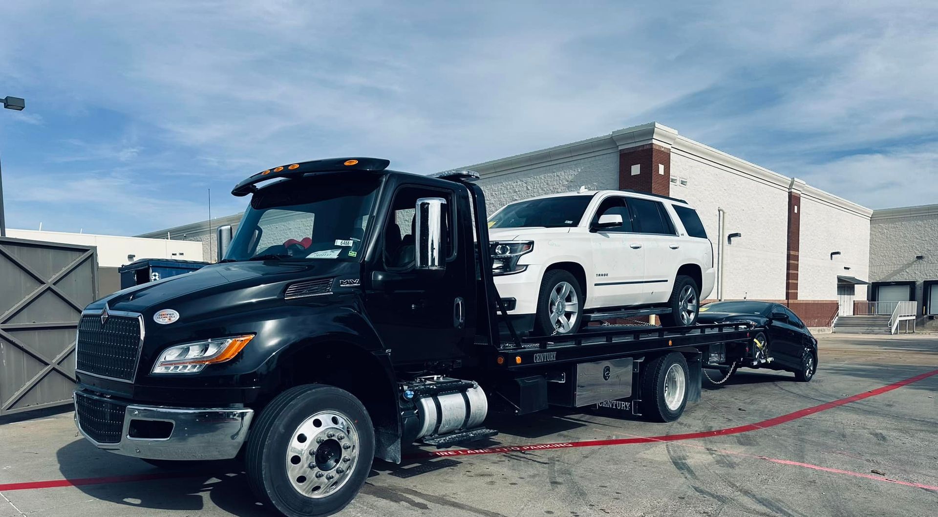 A tow truck is carrying a white suv and a black car.