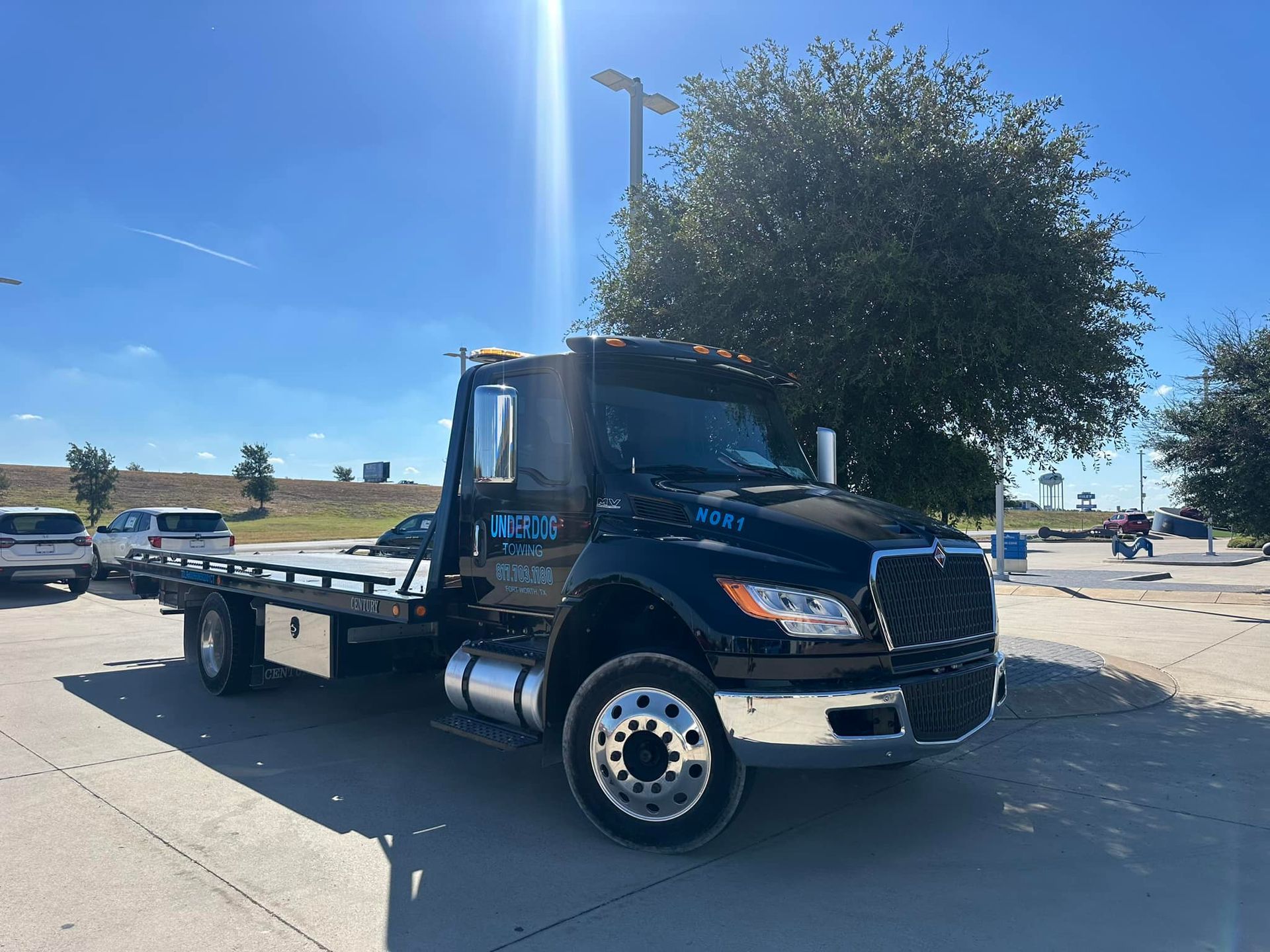 A black tow truck is parked in a parking lot next to a tree.