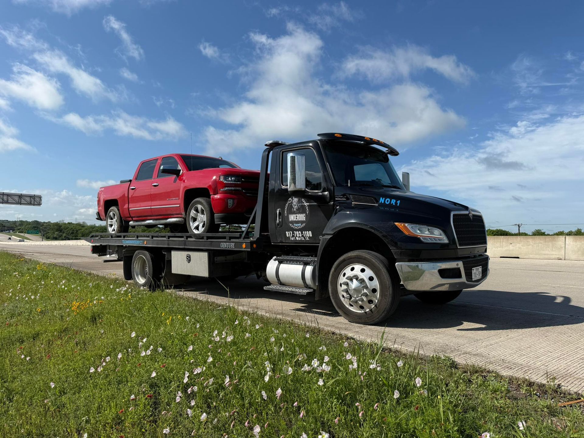 A tow truck is carrying a red truck on the back of it.