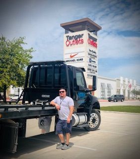A man is standing next to a tow truck in a parking lot.