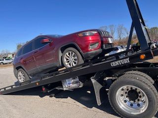 A red jeep is being towed by a century tow truck.