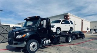 A tow truck is towing a white suv and a black car.