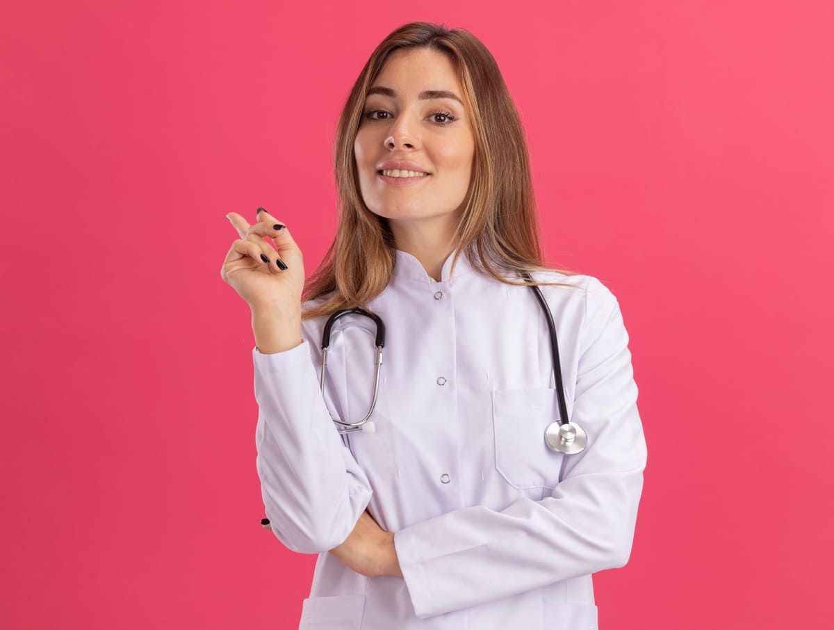 Jovem ginecologista sorridente usando roupão médico com pontos de estetoscópio ao lado isolados na p