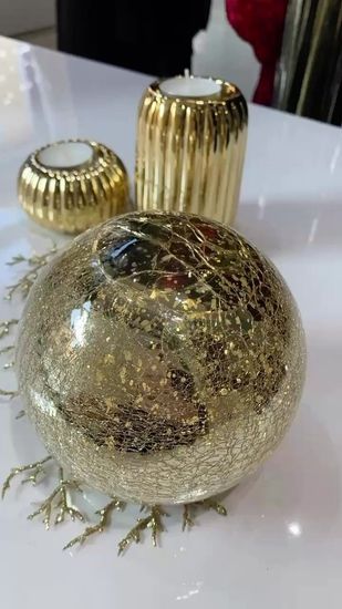 Portacandele dorati e sfera decorativa su una superficie bianca, forse un tavolo.