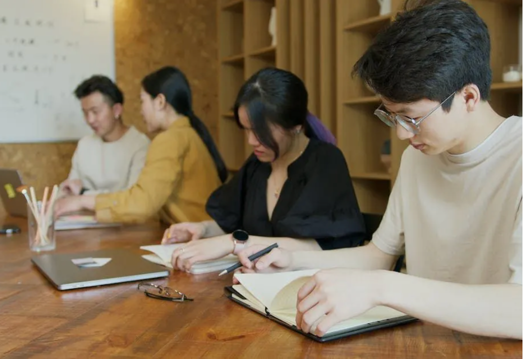 A group of people are sitting at a table with laptops and notebooks.