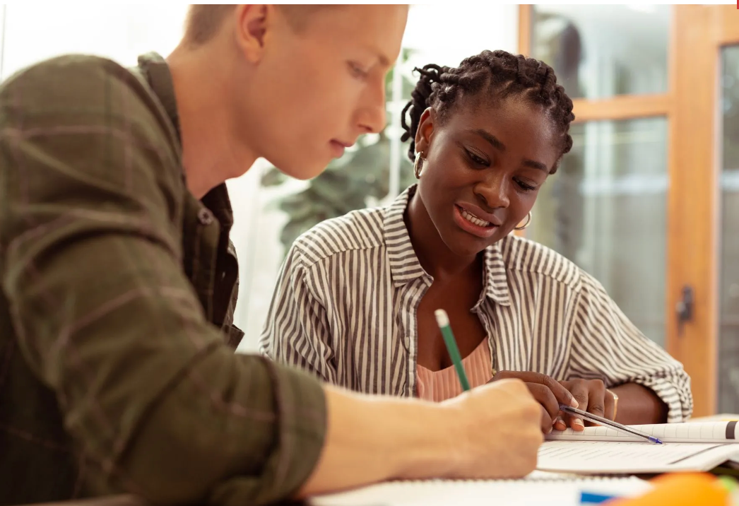 A man and a woman are sitting at a table writing on a piece of paper.