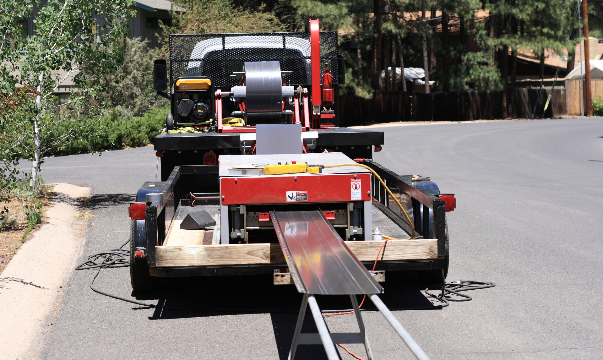 Metal sheet bending machine on a trailer, parked on a road.