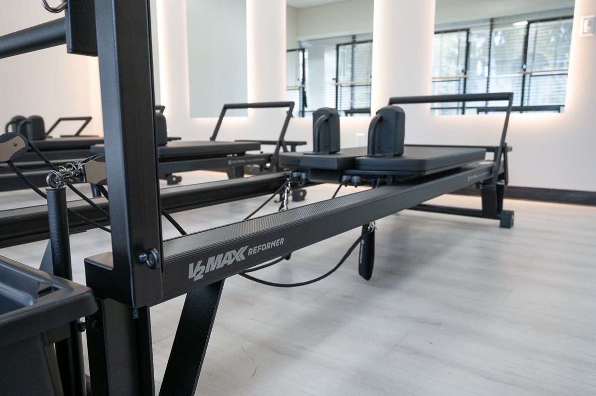 Black Pilates reformers in a bright studio with white columns and large windows.