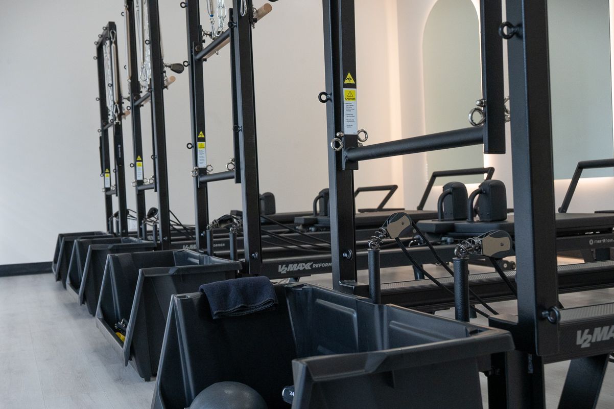 Row of black Pilates machines in a bright, modern studio.