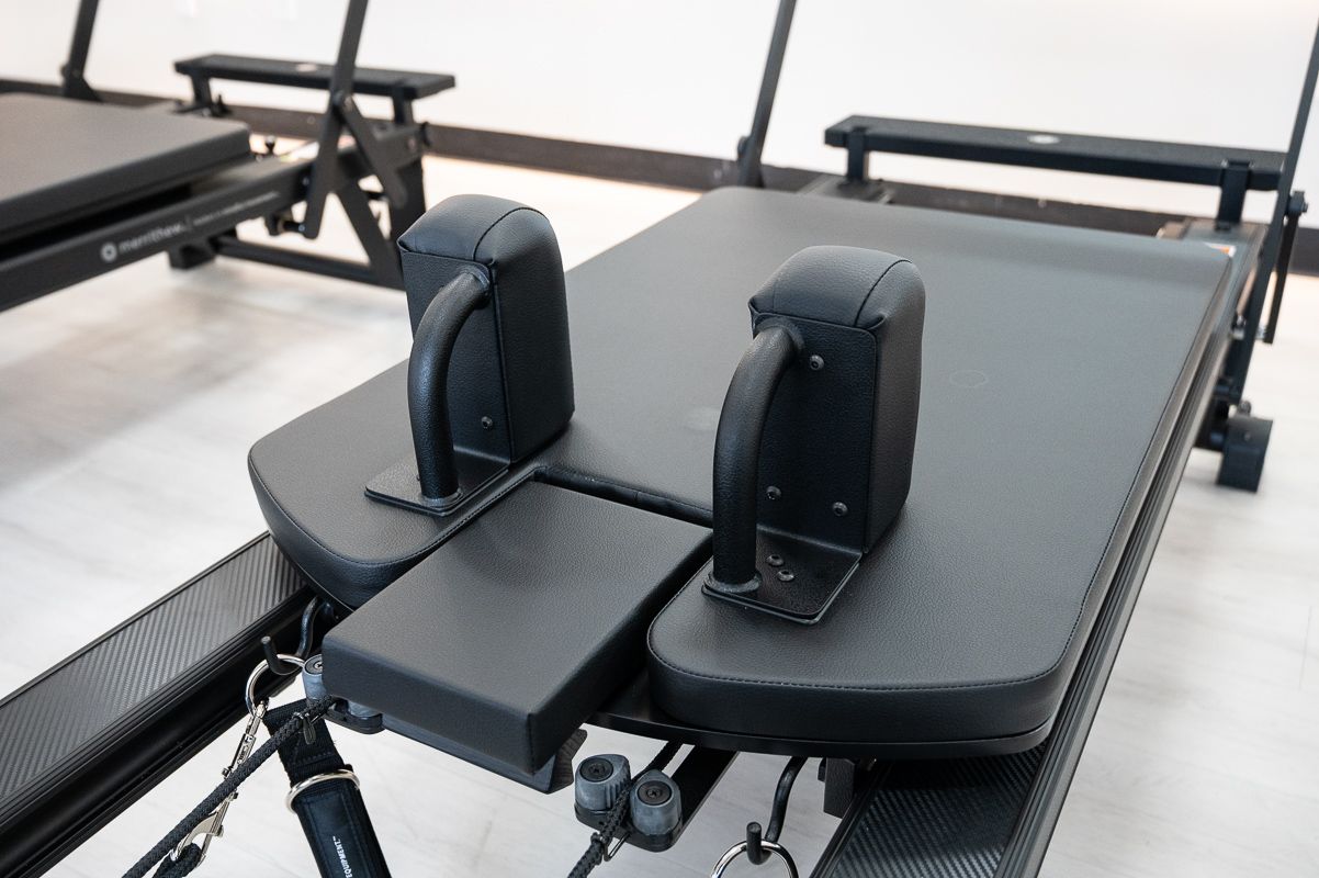 Pilates reformer machine with padded headrest and handles in a studio.
