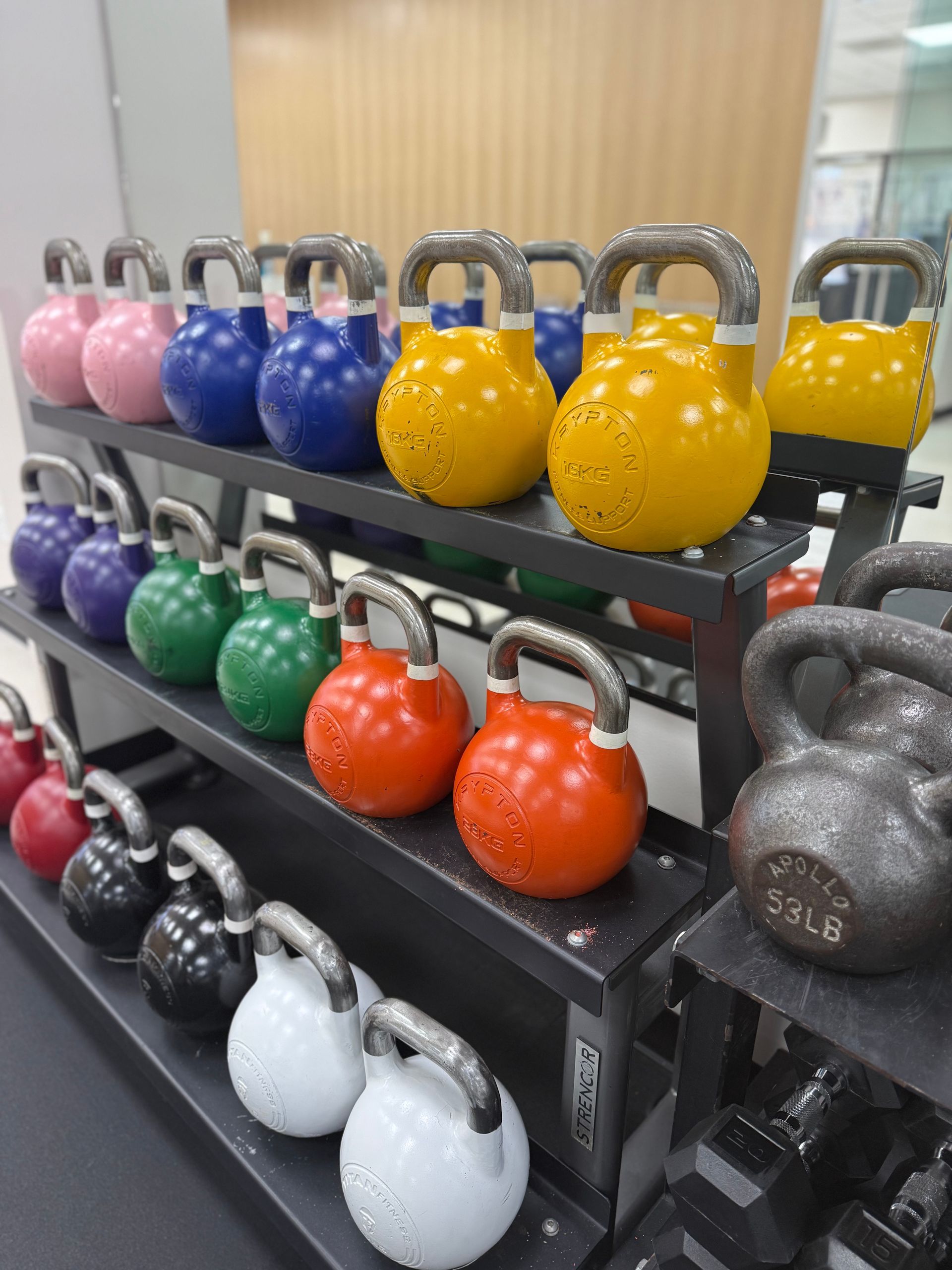 Colorful kettlebells on tiered black shelves in a gym setting.