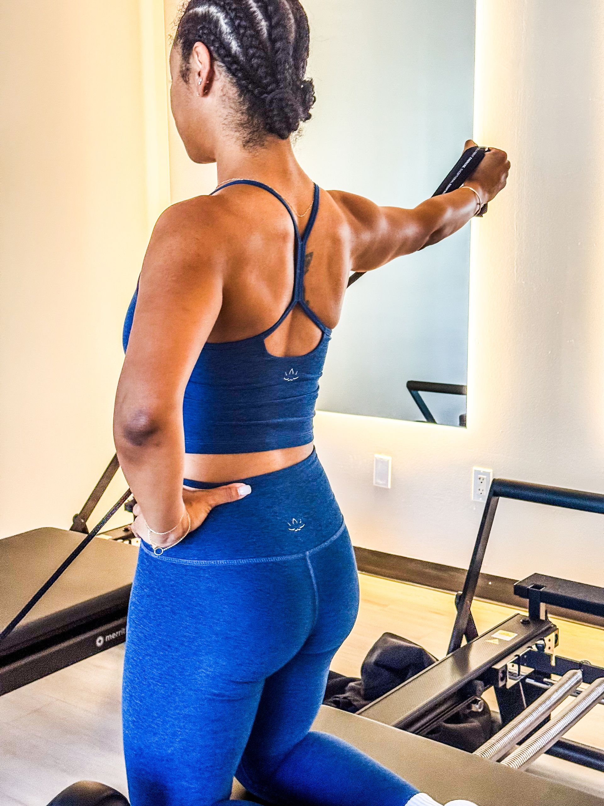 Woman doing pilates on a machine, wearing blue athletic wear, pulling on a handle.