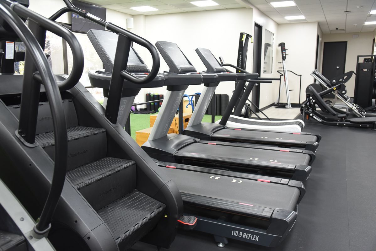 Man running on a treadmill in a gym, next to large windows.