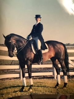 A woman is riding a brown horse in front of a white fence.