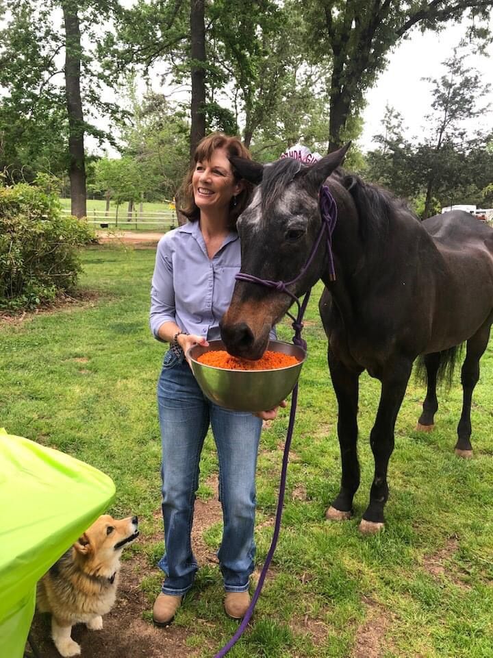 A woman is feeding a horse a bowl of food in a field.