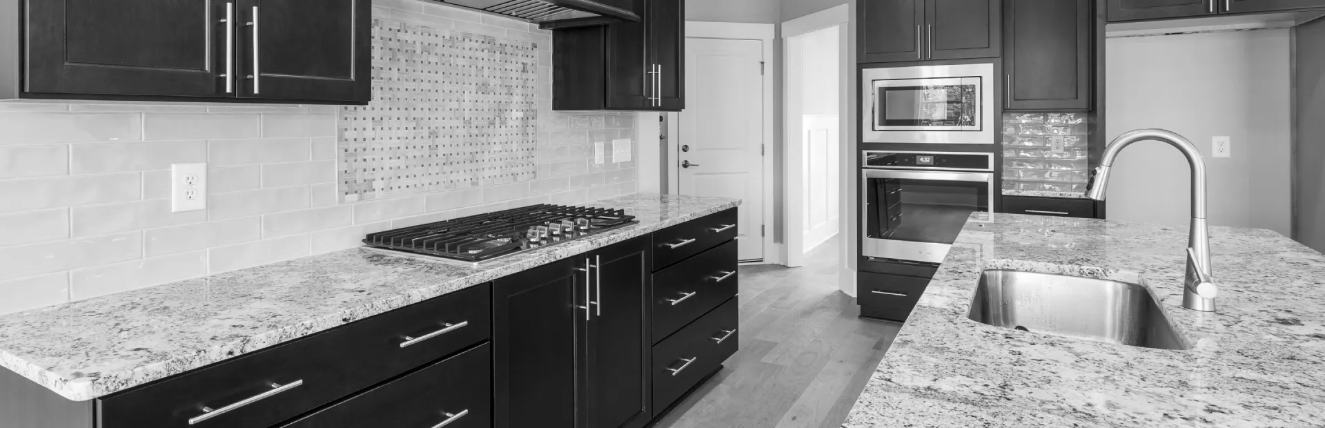 A black and white photo of a kitchen with granite counter tops and black cabinets.