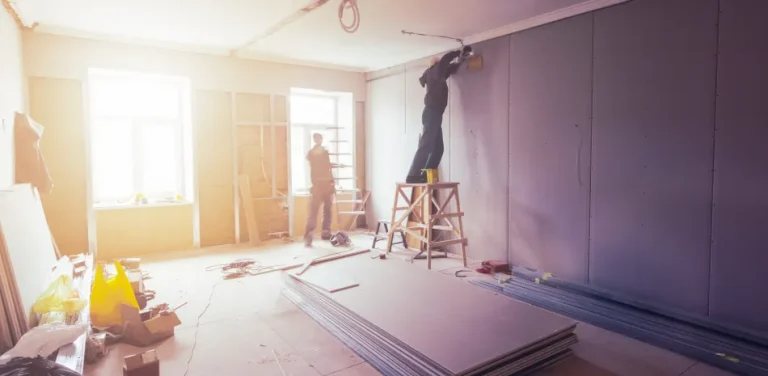 A man is standing on a ladder in a room under construction.