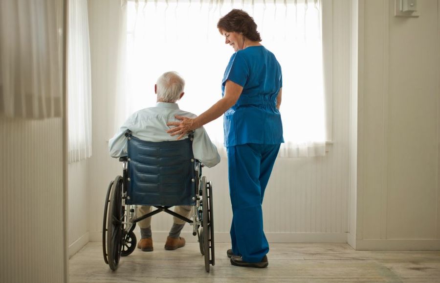 A nurse is standing next to an elderly man in a wheelchair.