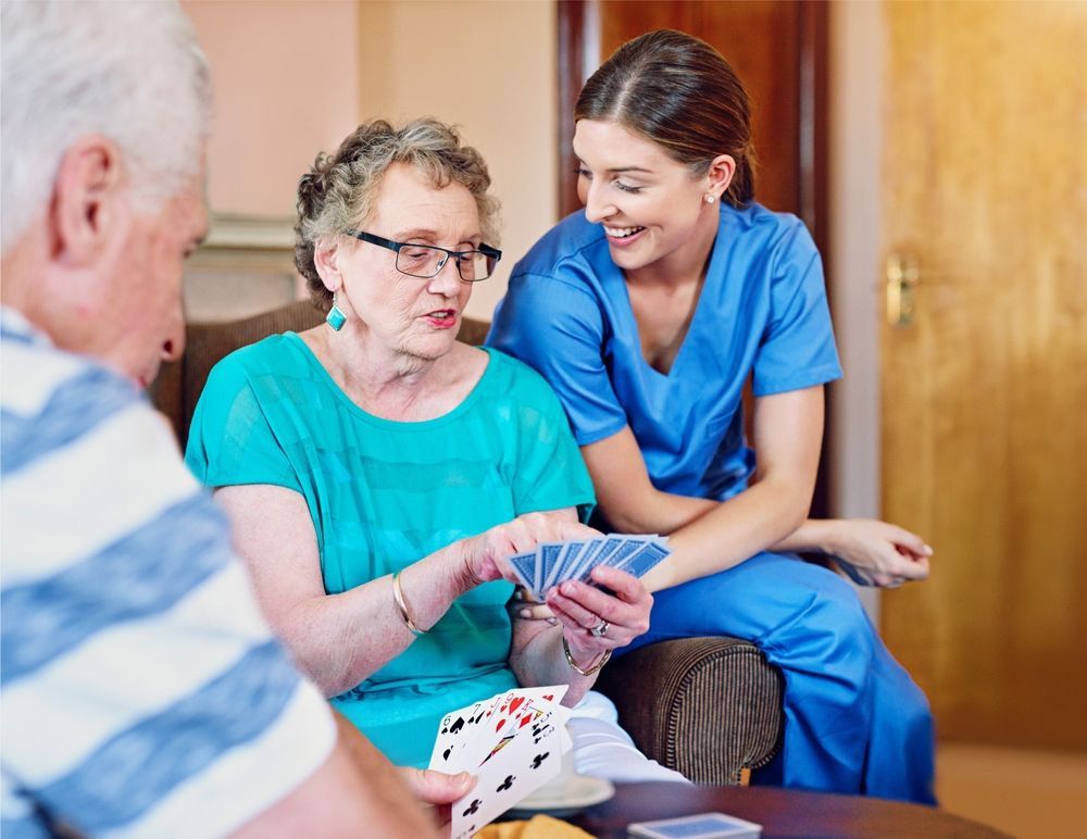 A nurse is helping an elderly woman play a game of cards.
