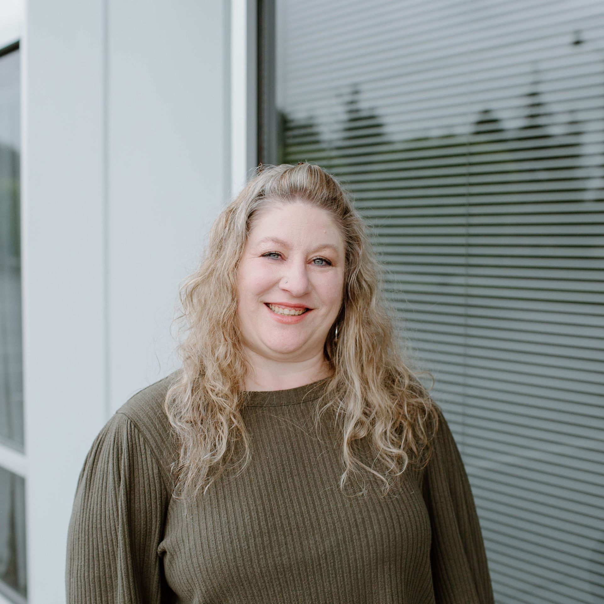 A woman in a green sweater is smiling in front of a window.
