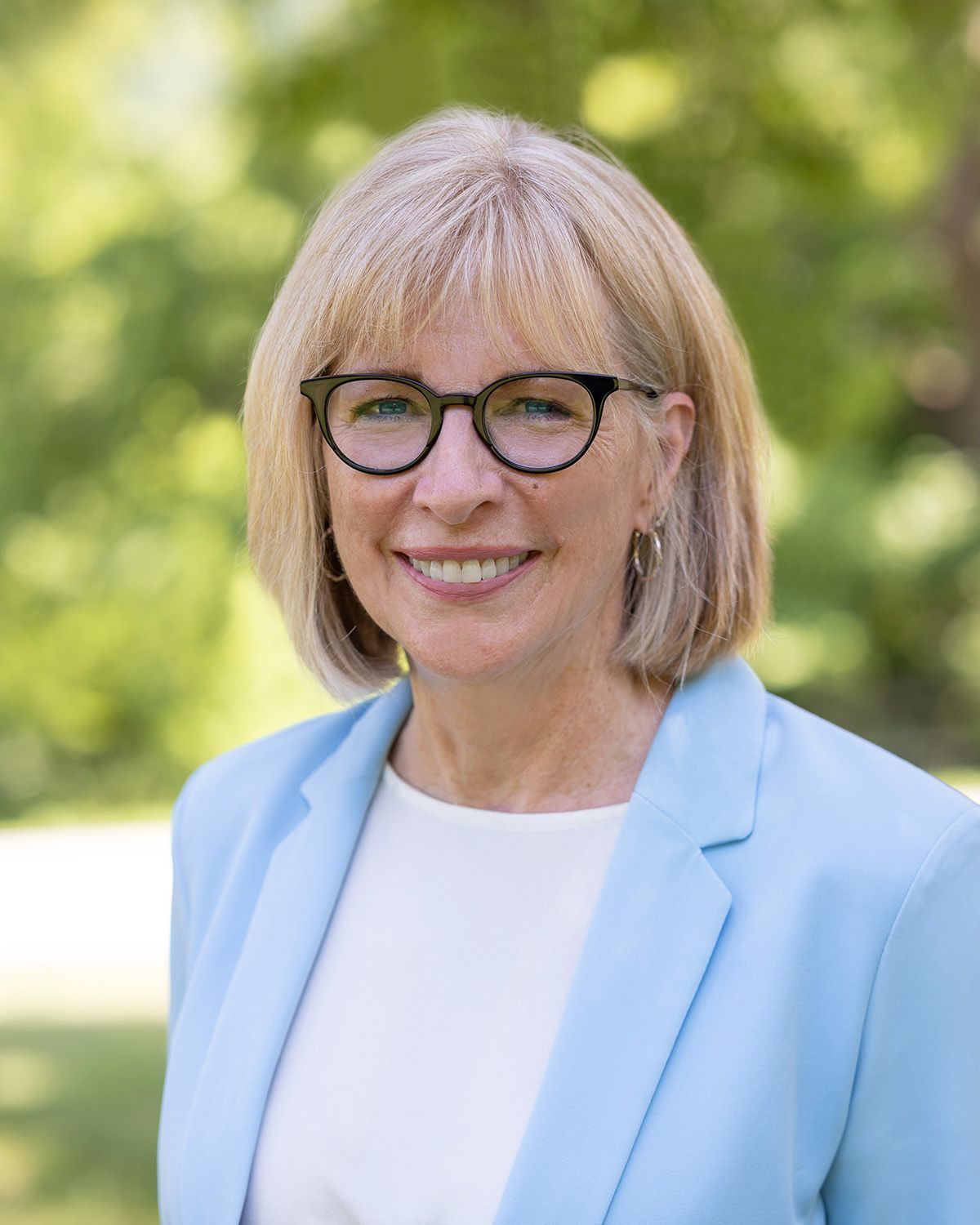 A woman wearing glasses and a pink jacket is smiling for the camera.
