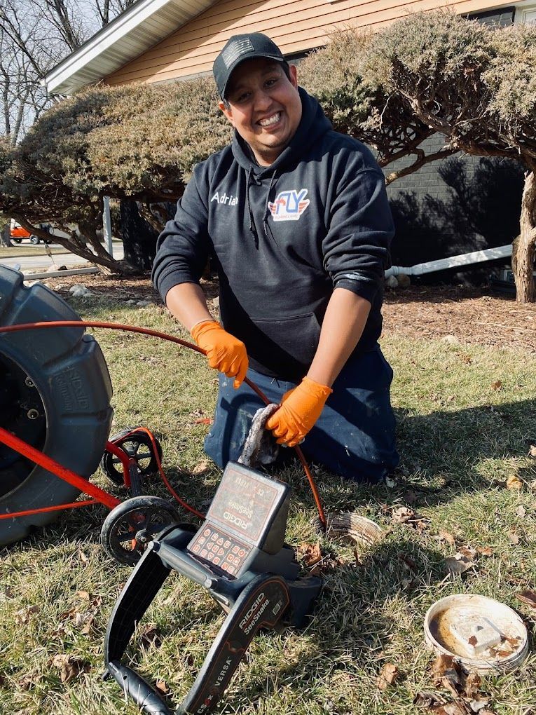 A man is kneeling down in the grass next to a drain camera.