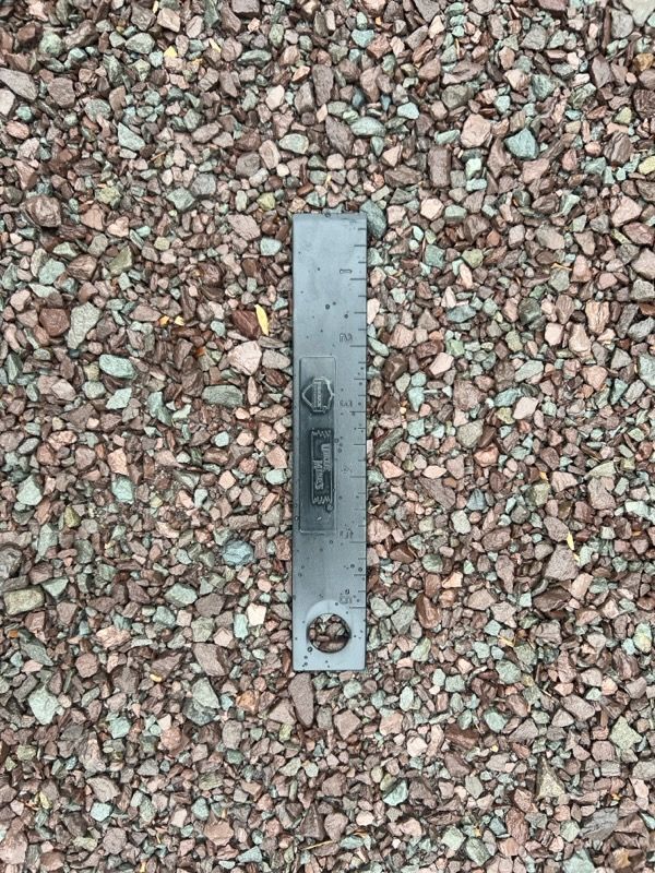 Gravel with a black ruler centered; gravel is reddish-brown and gray.