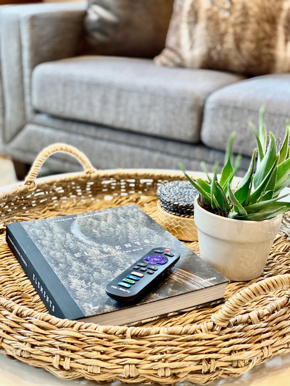 A wicker tray with a book, remote control, and potted plant on it.