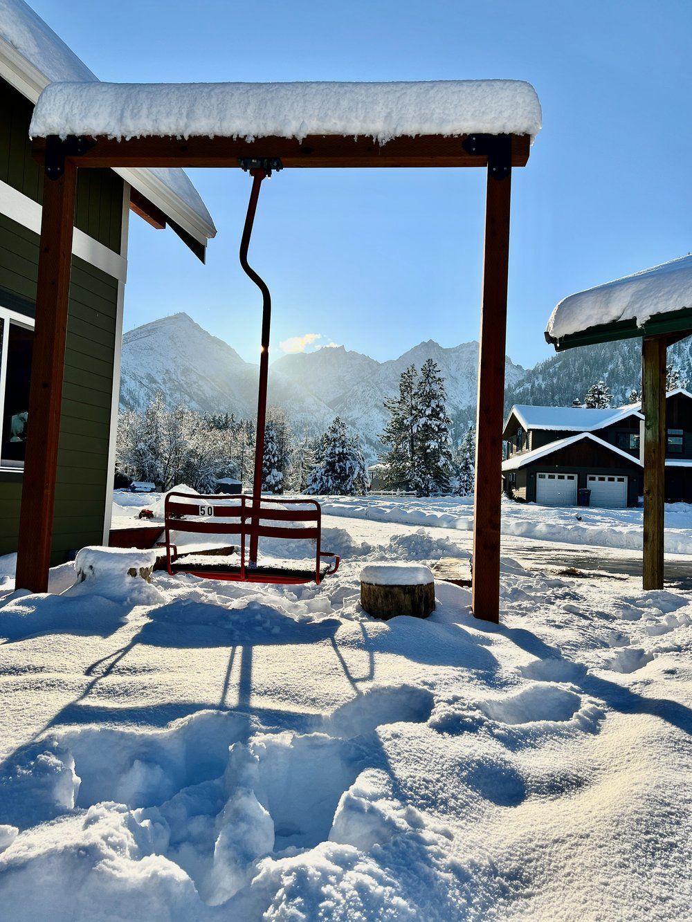 A ski lift swing hanging above the snow in front of a house.