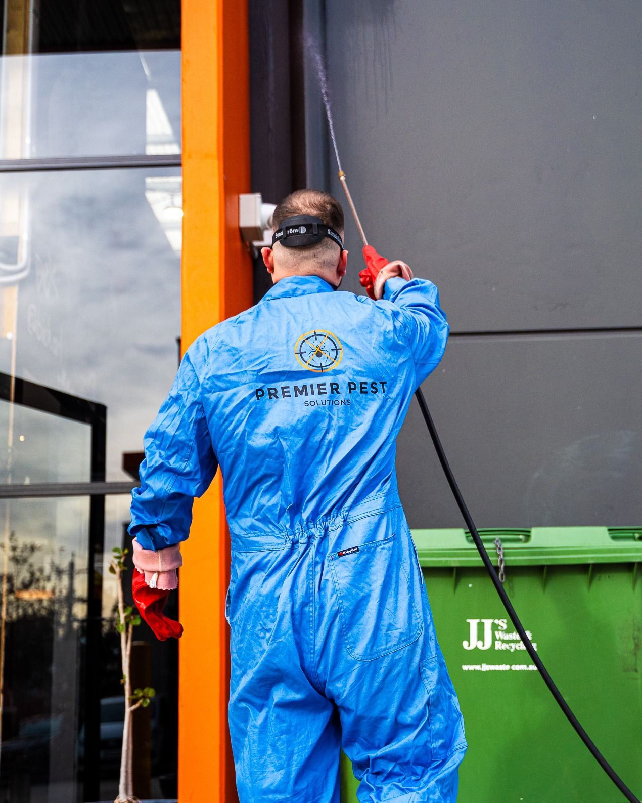 Man in Blue Coveralls Pressure Washing Building Exterior — Premier Pest Control Wollongong In Macarthur, NSW