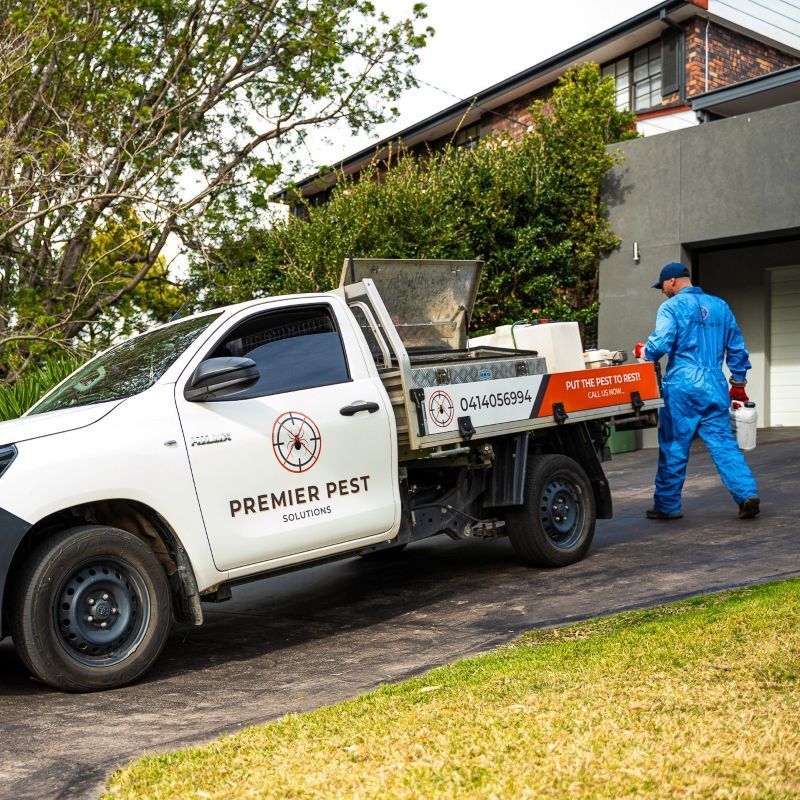 Pest control worker in blue suit exits Premier Pest Services truck parked in front of a house — Premier Pest Control Wollongong In Wollongong, NSW